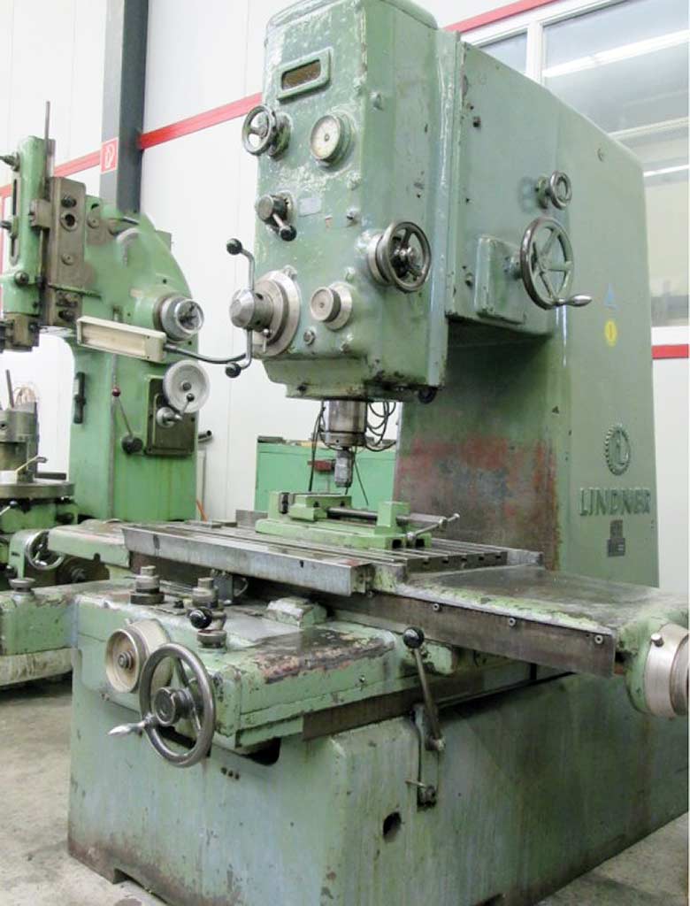 Grün lackierte Ständerbohrmaschine von Lindner, der Herstellername im Ständer gegossen, mit vertikalem Spindelkopf über einem T-Nuten-Tisch