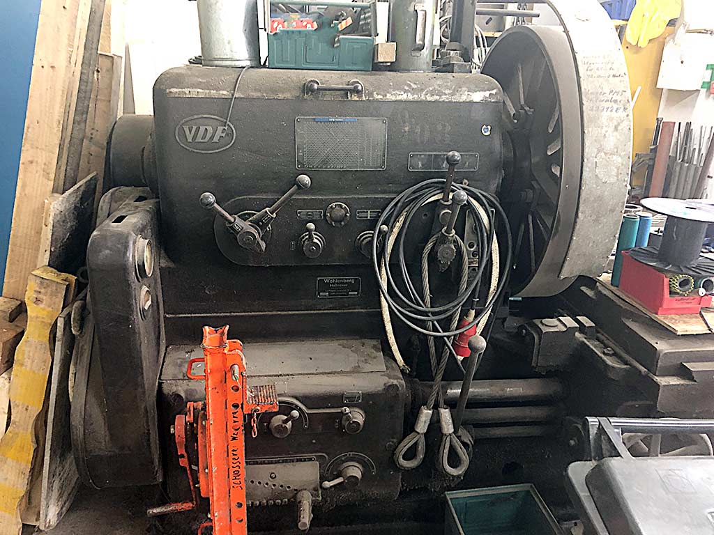 Spindelstock einer Wohlenberg-Drehmaschine mit VDF-Emblem und Typenschild Wohlenberg Hannover, dahinter ein großes Speichenrad, über der Maschine liegende Hebeseile